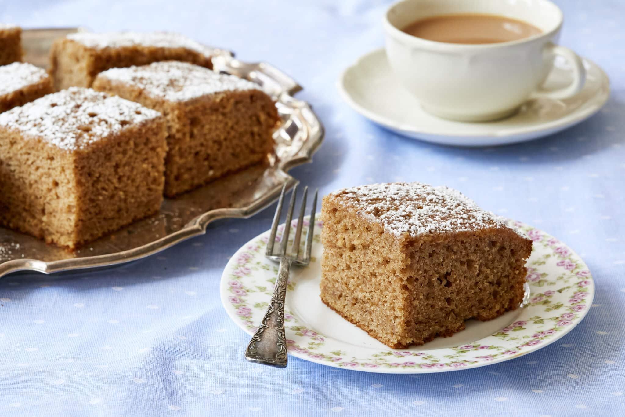 Slice of spice cake with a fork on a plate and a cup of tea